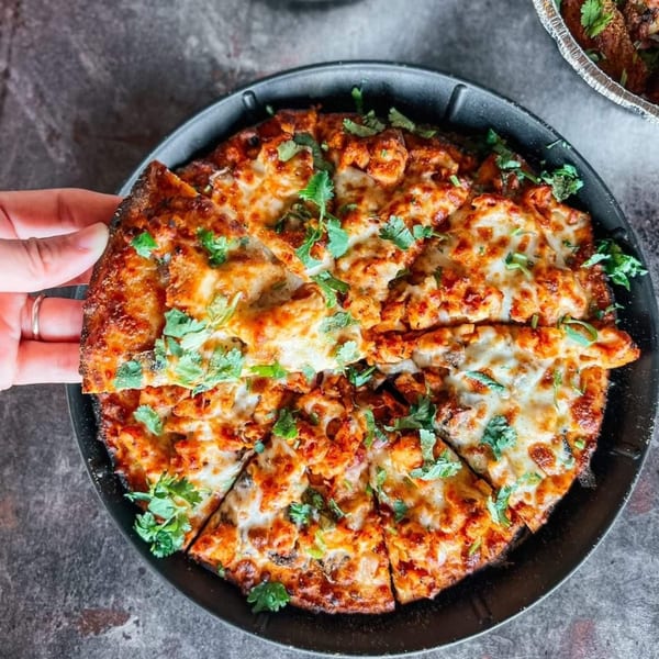 A hand reaching for a slice of Parktown Pizza's chicken tikka pizza, topped with cilantro.