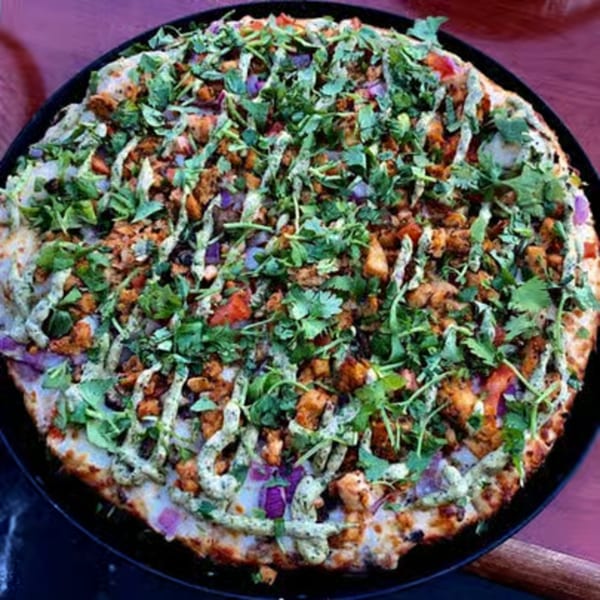 Parktown Pizza's chicken tikka pizza, topped with cilantro, red onions, and green sauce.