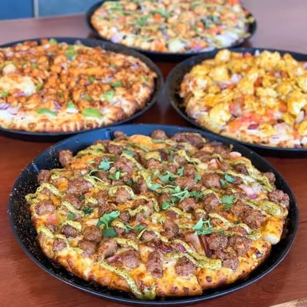 Four Parktown Pizza pizzas with various toppings, including chicken, vegetables, and a green sauce.