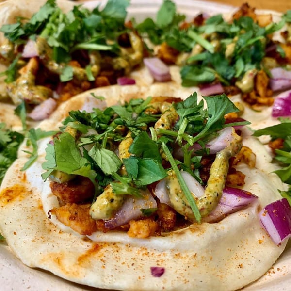 Close-up of three Parktown Pizza tacos with chicken, red onion, cilantro, and a creamy green sauce.