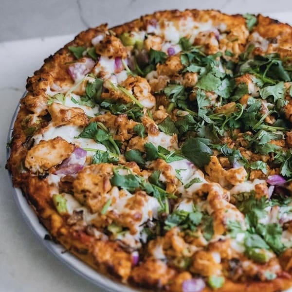A Parktown Pizza with chicken, red onions, and cilantro on a white plate.